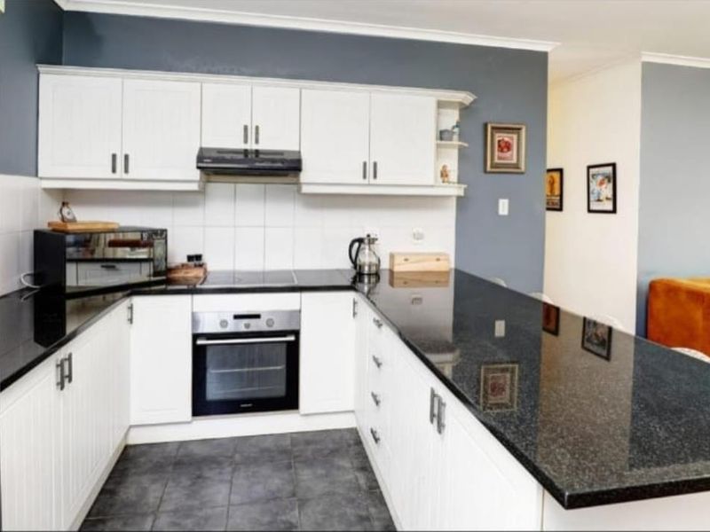 A functional kitchen featuring white cabinetry, black granite countertops, a built-in oven, and a breakfast bar peninsula.