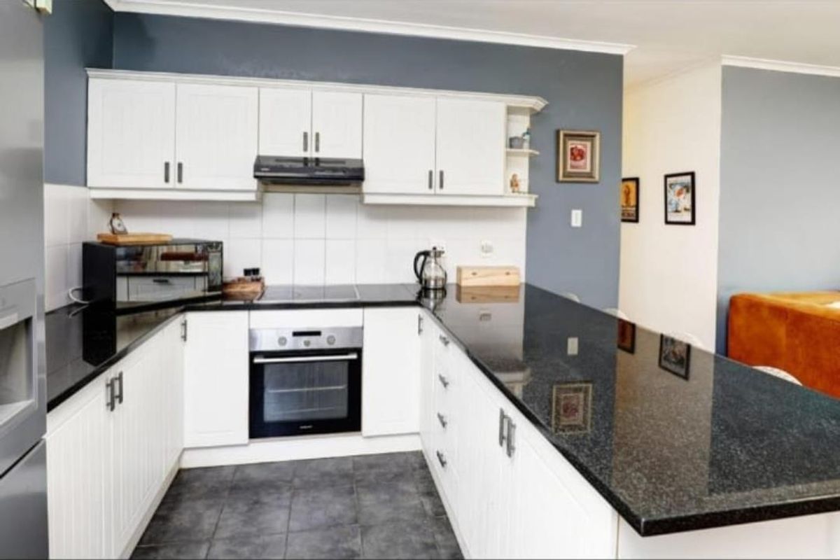 A functional kitchen featuring white cabinetry, black granite countertops, a built-in oven, and a breakfast bar peninsula.