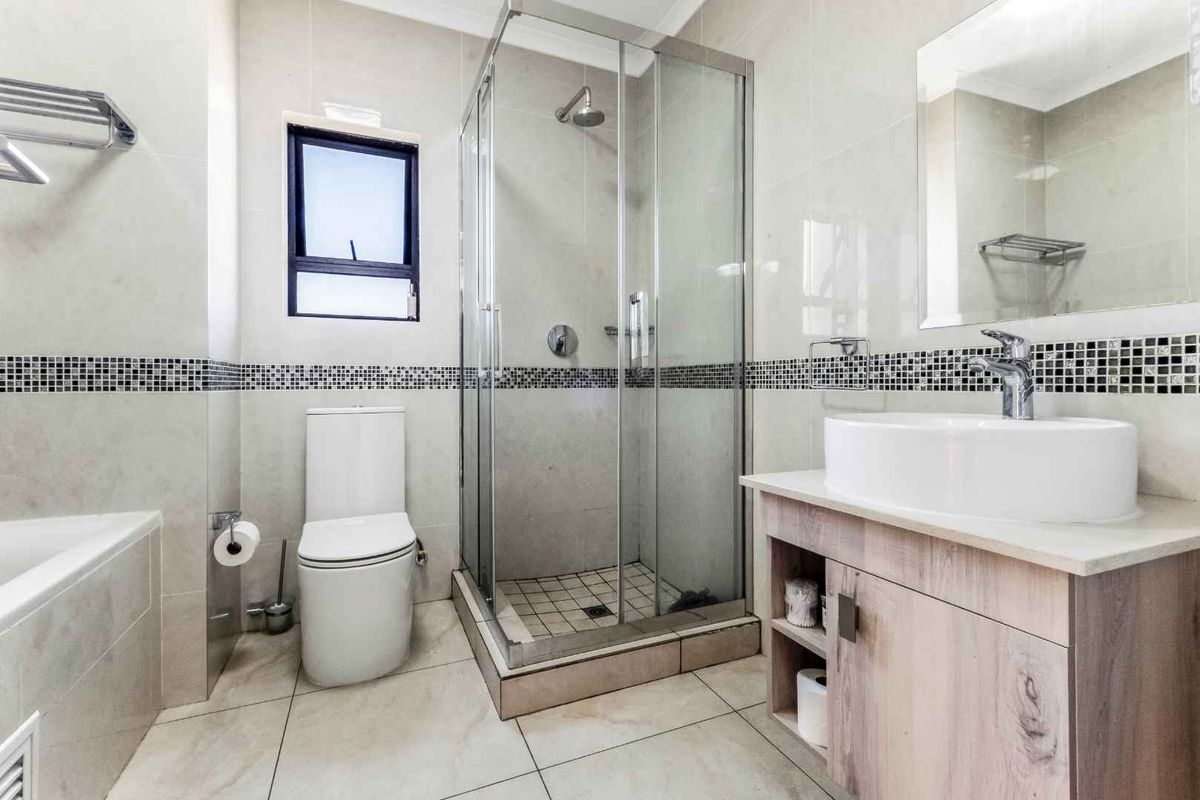 A modern bathroom featuring a glass-enclosed shower, a separate bathtub, a vanity with a vessel sink, and neutral wall and floor tiling.