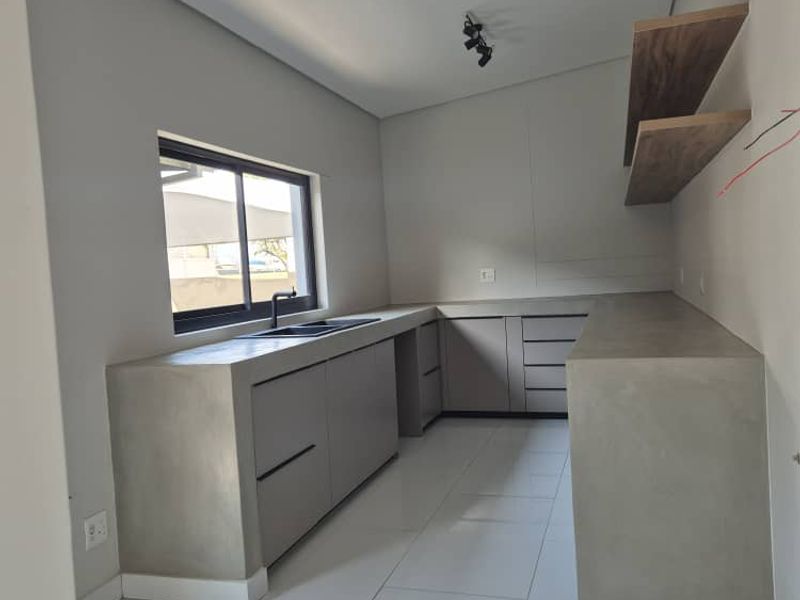Modern kitchen featuring concrete countertops, sleek cabinetry, floating shelves, and tiled flooring, offering a contemporary minimalist aesthetic ready for final finishing touches.