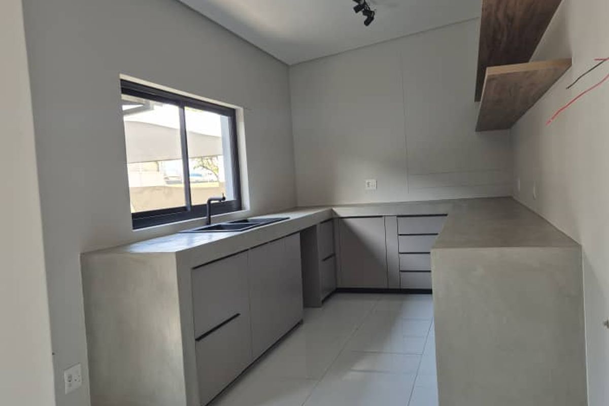 Modern kitchen featuring concrete countertops, sleek cabinetry, floating shelves, and tiled flooring, offering a contemporary minimalist aesthetic ready for final finishing touches.