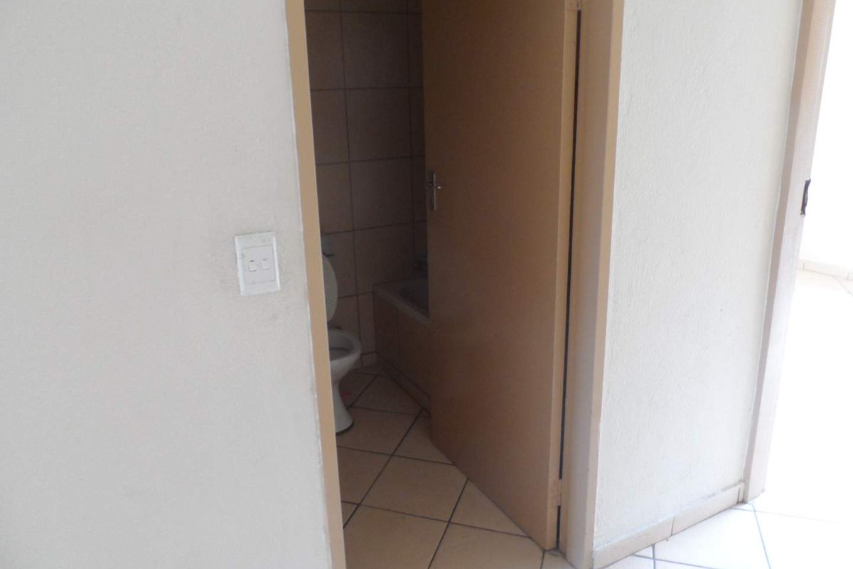 A view into a functional bathroom featuring tiled flooring, tiled walls, a bathtub, and a toilet, accessible via a standard interior door.