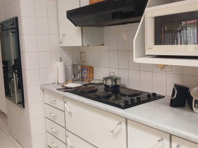 A functional kitchen featuring white cabinetry, tiled splashbacks, a built-in oven, electric hob, and integrated microwave.