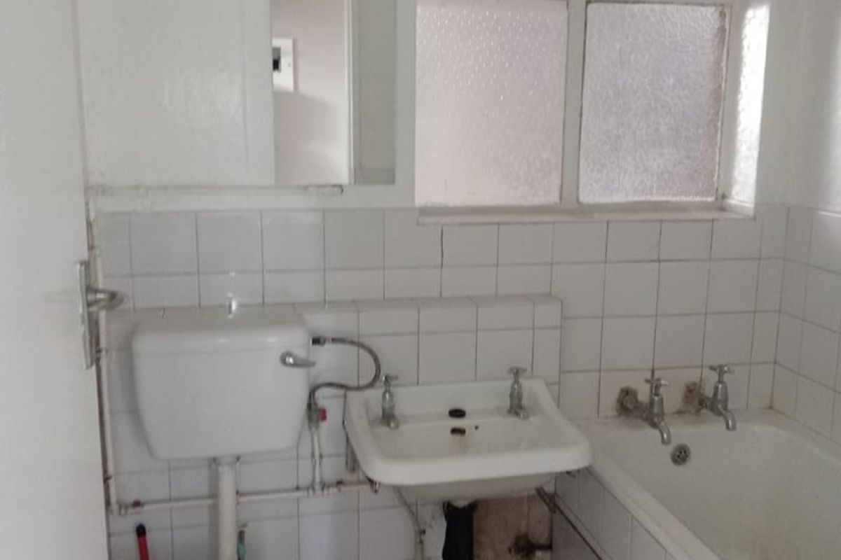 A dated bathroom featuring a standard bathtub, washbasin, and toilet with white wall tiling and a window for natural light.