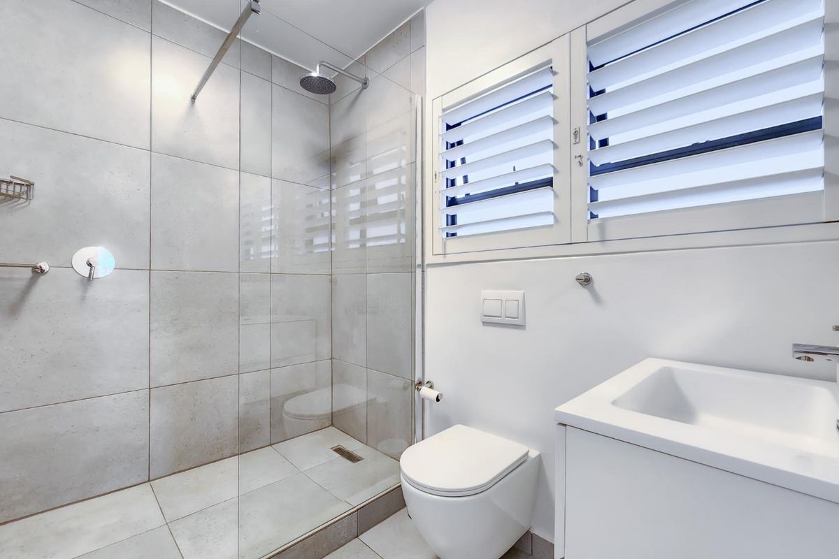 Modern bathroom featuring a walk-in shower with glass screen, wall-mounted toilet, vanity basin, and neutral tiled finishes.