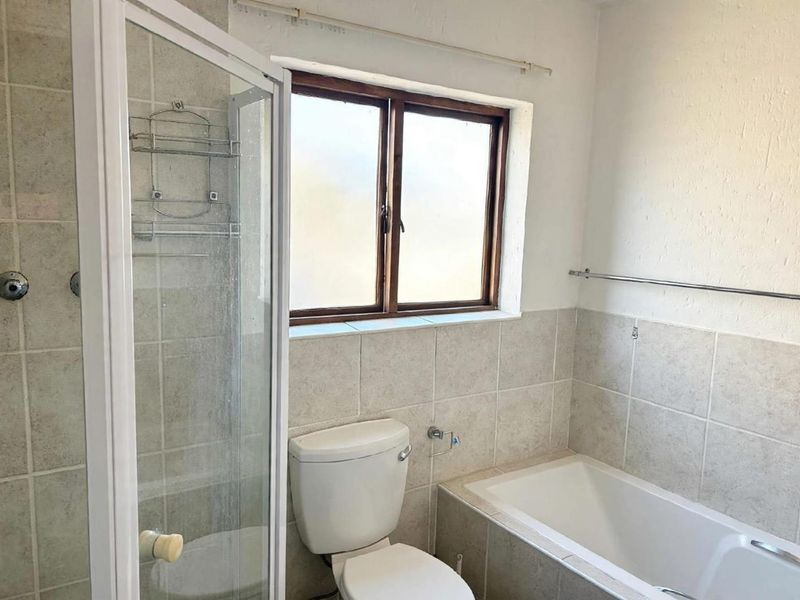 A functional bathroom featuring a shower enclosure, bathtub, and toilet with neutral wall tiling and a window for natural light.