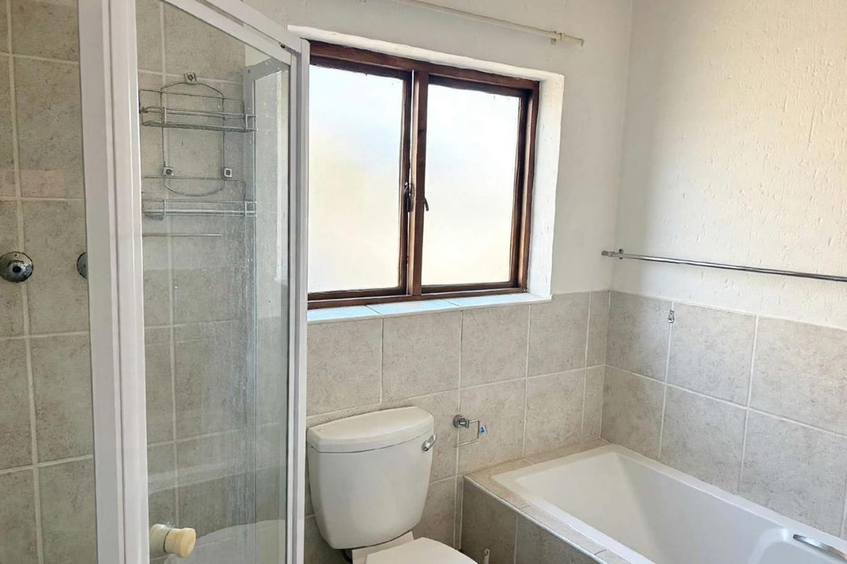 A functional bathroom featuring a shower enclosure, bathtub, and toilet with neutral wall tiling and a window for natural light.