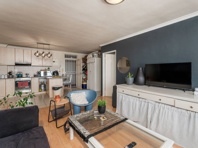 Open-plan living area featuring a functional kitchen with built-in cabinetry, oven, and hob, seamlessly flowing into the lounge space with laminate flooring.