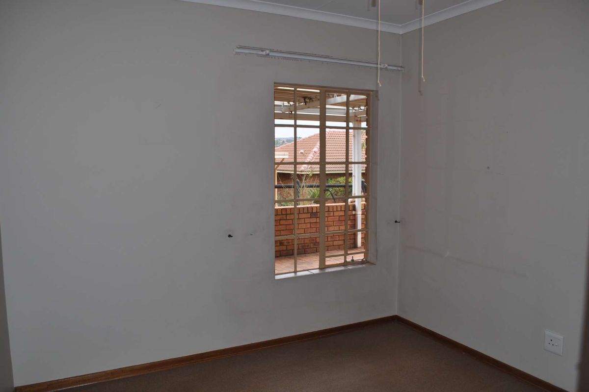 An empty bedroom featuring neutral walls, carpeted flooring, and a window with security bars overlooking a patio area.