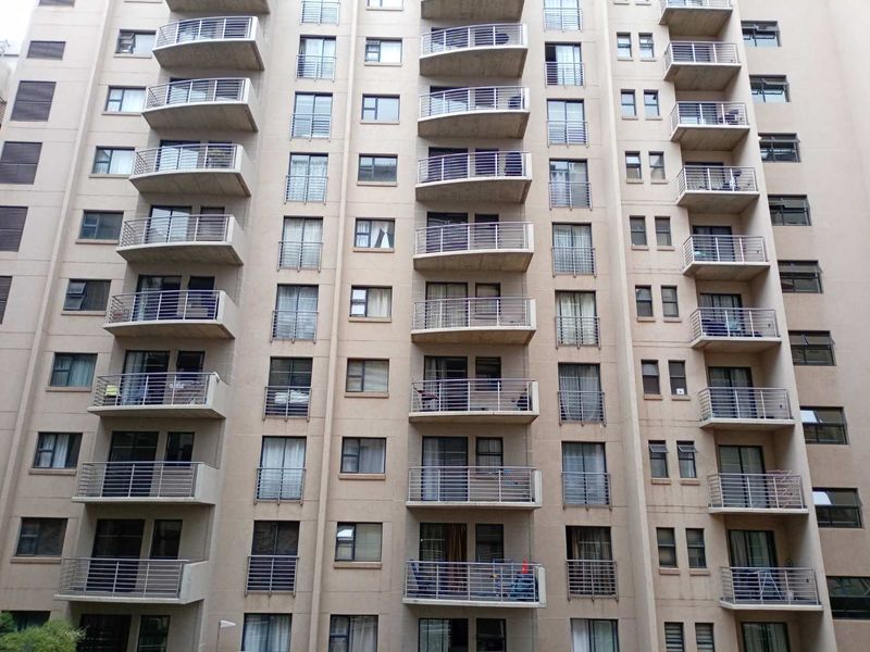 A multi-story residential building facade featuring uniform balconies with metal railings and various window configurations.