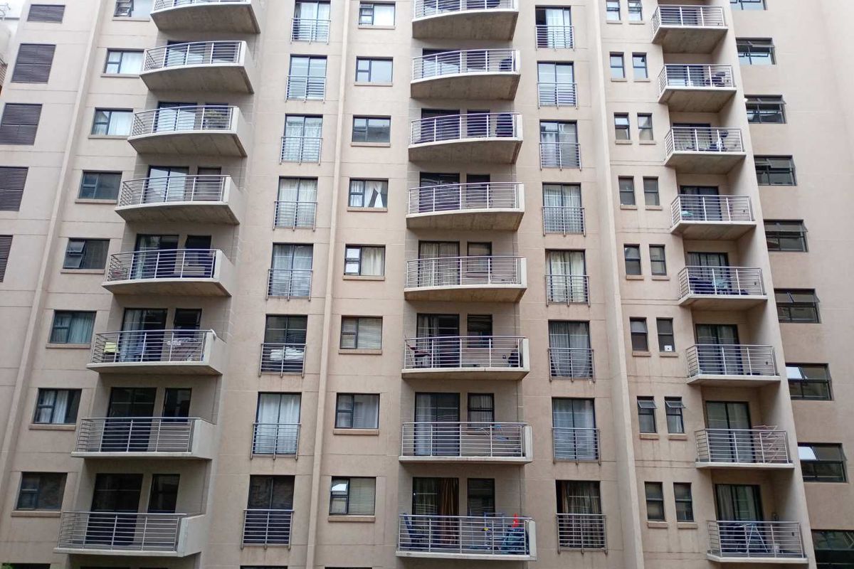 A multi-story residential building facade featuring uniform balconies with metal railings and various window configurations.