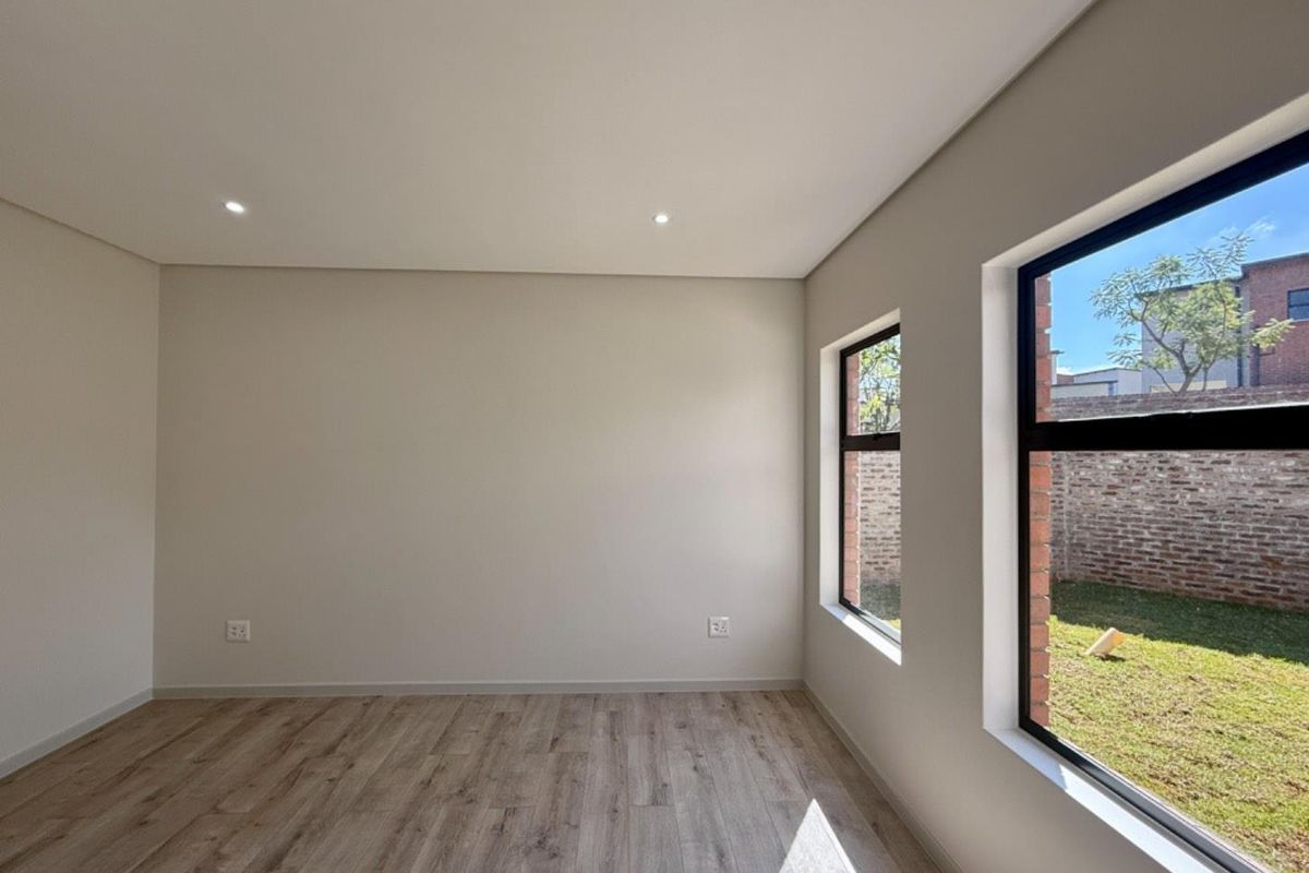 A bright, empty bedroom featuring modern laminate flooring, recessed downlights, and large windows overlooking the garden.