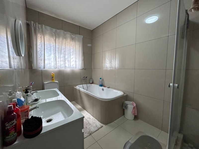 A functional bathroom featuring a double vanity, a built-in bathtub, and a separate shower enclosure with neutral wall and floor tiling.