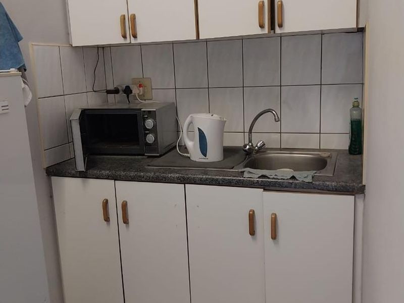 A compact kitchenette featuring white built-in cabinetry, a stainless steel sink, and tiled backsplash, suitable for a small industrial or office utility space.