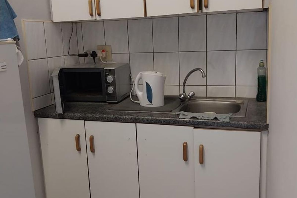 A compact kitchenette featuring white built-in cabinetry, a stainless steel sink, and tiled backsplash, suitable for a small industrial or office utility space.