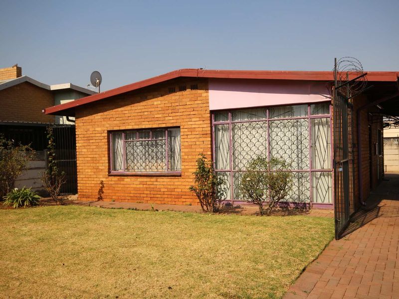 Front view of a face brick house featuring security bars on windows, a paved driveway, and perimeter security fencing.