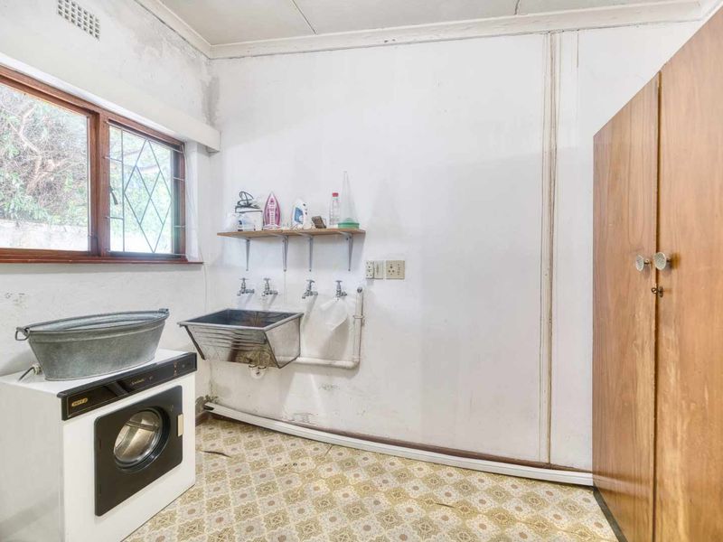 A functional laundry room featuring a stainless steel sink, plumbing connections, and built-in storage, requiring cosmetic updates to improve the overall condition.