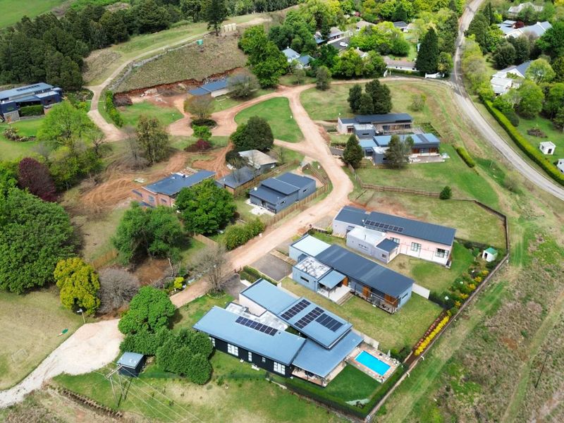 Aerial view of a residential estate featuring multiple modern homes, solar installations, swimming pools, and expansive landscaped grounds.