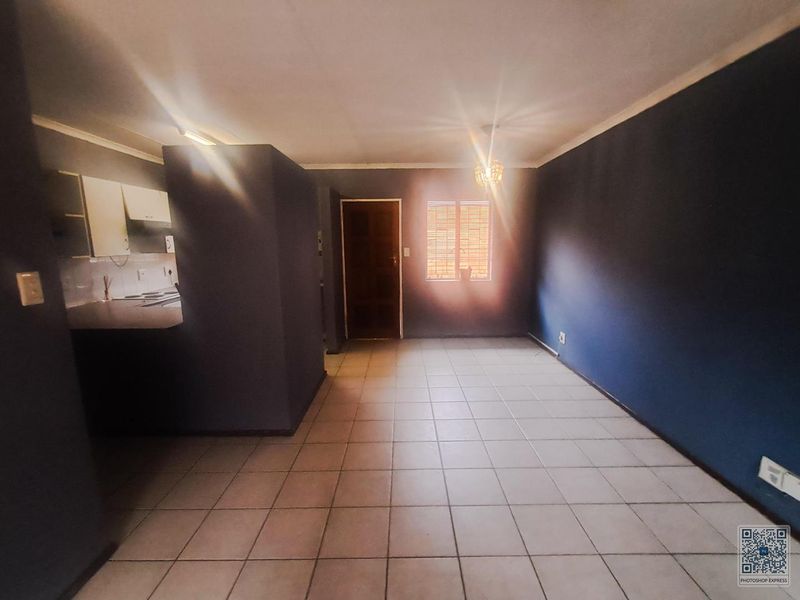 An open-plan living and kitchen area featuring tiled flooring, dark blue walls, and built-in kitchen cabinetry, offering a functional and versatile living space.