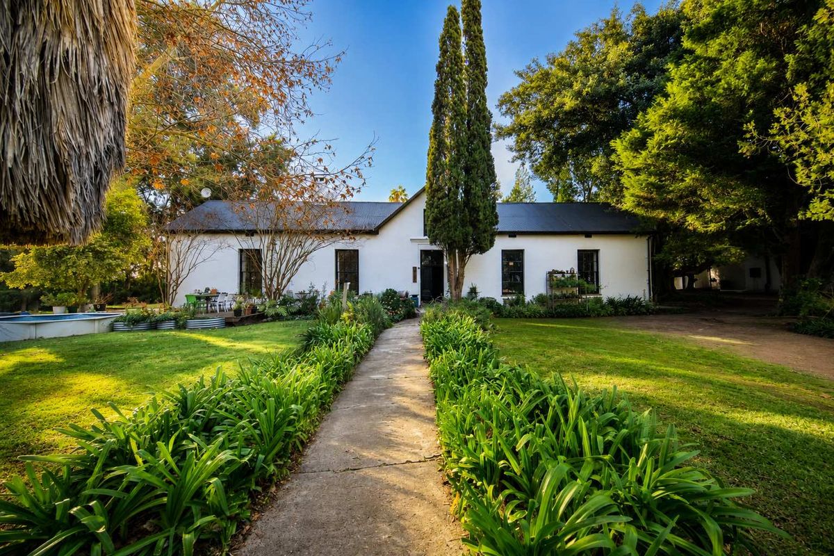 A charming rear view of the property featuring a well-maintained garden, a central concrete pathway, and mature landscaping leading to the main building structure.