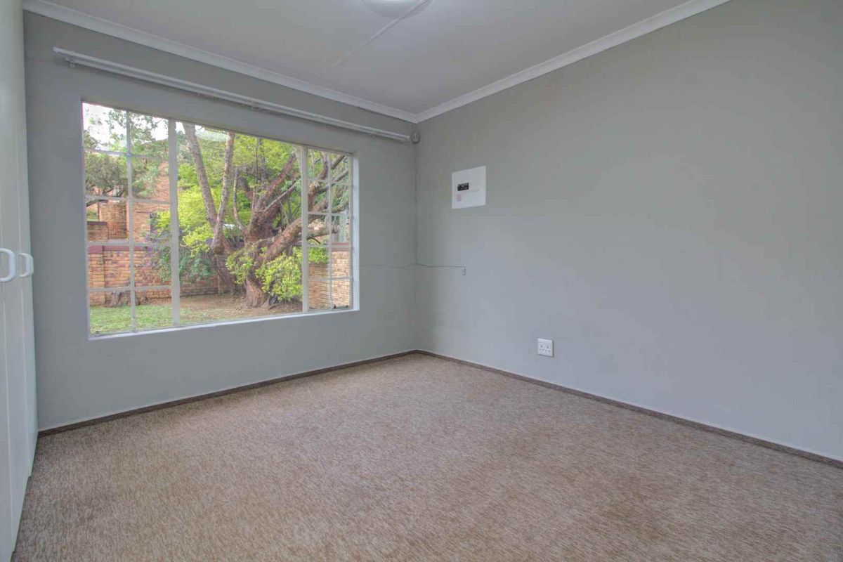 A vacant bedroom featuring neutral wall paint, carpeted flooring, and a large window overlooking the garden area.