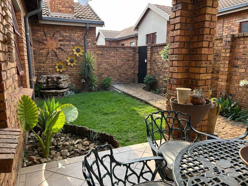 A private rear courtyard featuring a tiled patio, brick pillars, a small lawn, and a stone water feature enclosed by brick boundary walls.