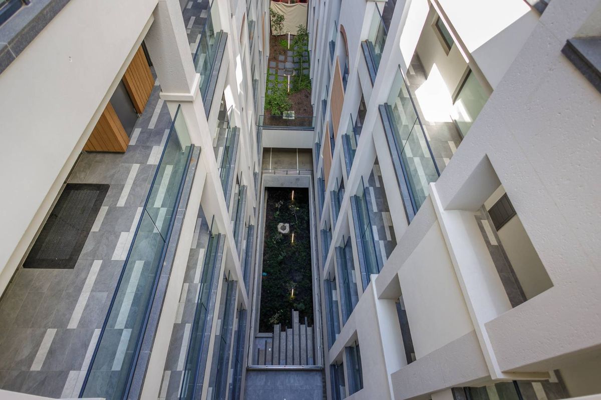 An elevated view looking down into the central atrium and light well of a modern apartment complex, featuring glass balustrades and landscaped garden beds.