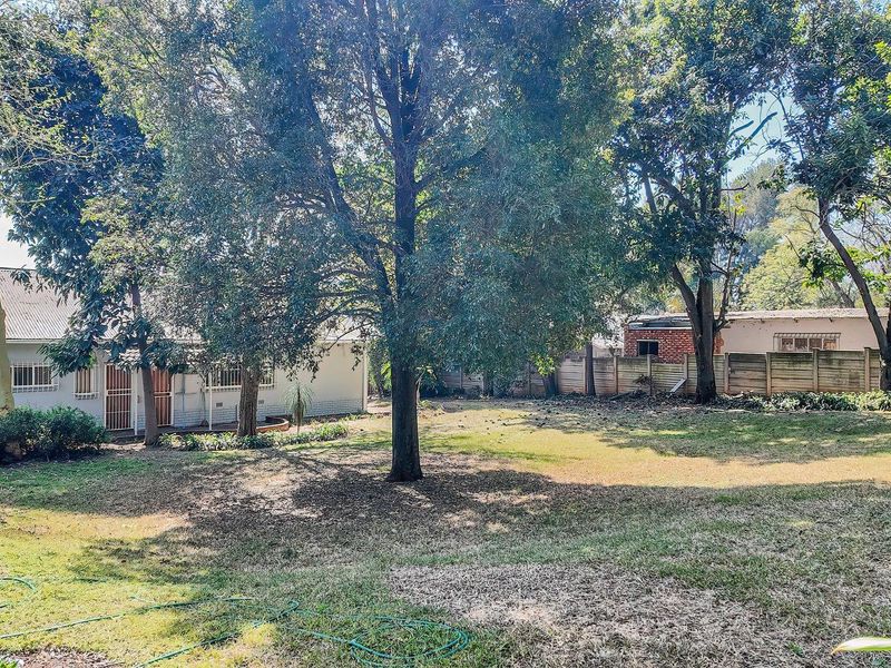 A spacious rear garden featuring mature trees, a precast concrete boundary wall, and a view of the rear building elevation with security bars.