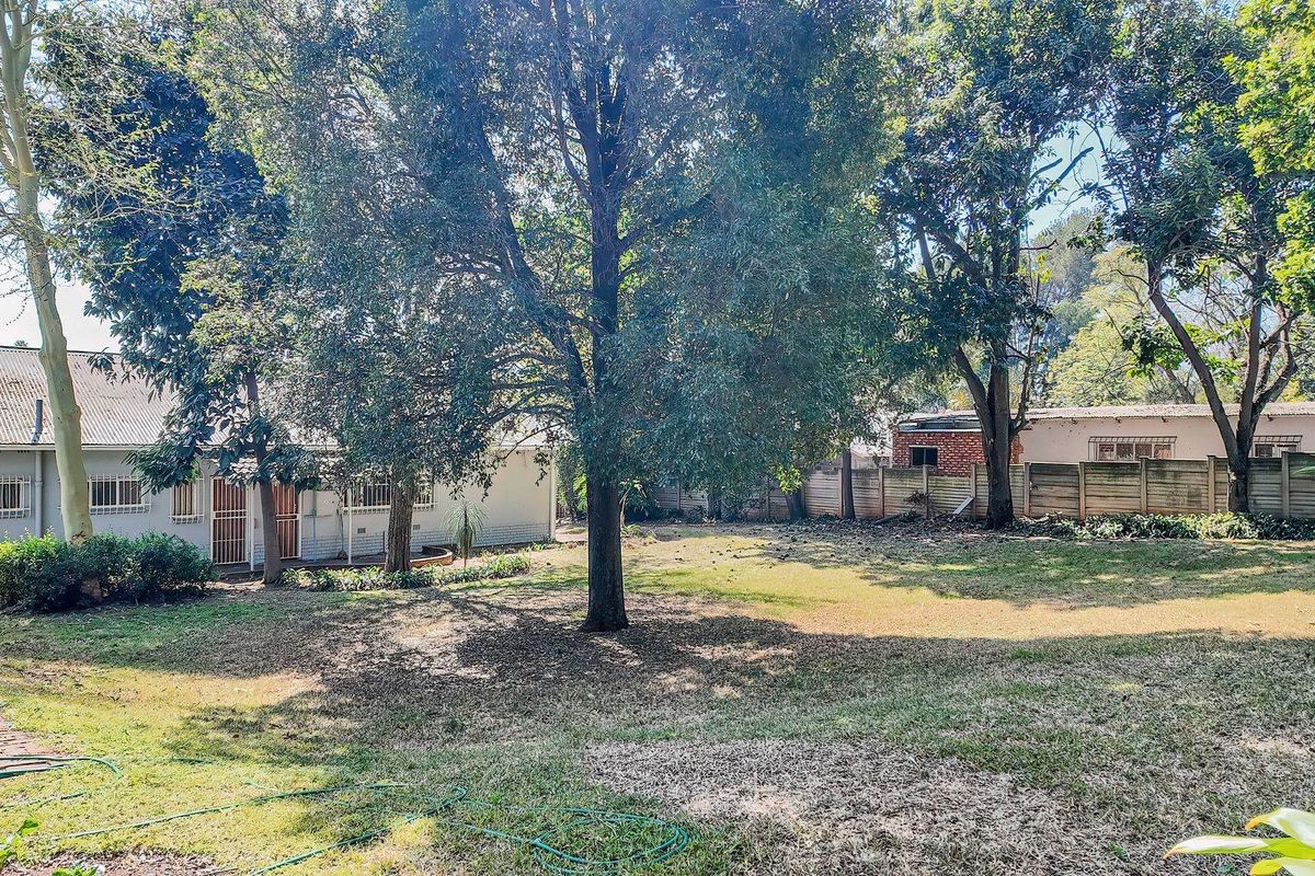 A spacious rear garden featuring mature trees, a precast concrete boundary wall, and a view of the rear building elevation with security bars.