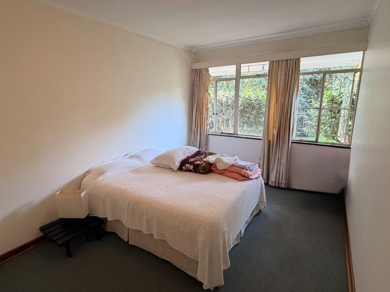 A functional bedroom featuring large windows that provide natural light and views of the garden, finished with carpeted flooring.
