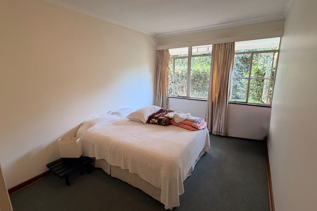 A functional bedroom featuring large windows that provide natural light and views of the garden, finished with carpeted flooring.