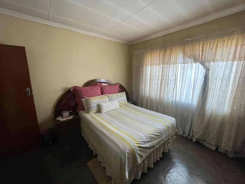 A bedroom featuring neutral walls, a large window with curtains, and a standard door, offering a functional space ready for modernization.