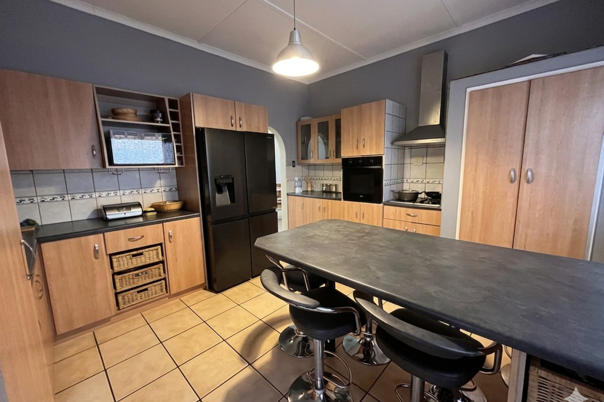A functional kitchen featuring light wood-tone cabinetry, dark countertops, a built-in oven, extractor fan, and a central island with breakfast bar seating.