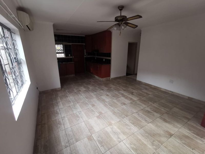 An open-plan living and kitchen area featuring tiled flooring, a ceiling fan, air conditioning, and built-in kitchen cabinetry with security bars on the windows.