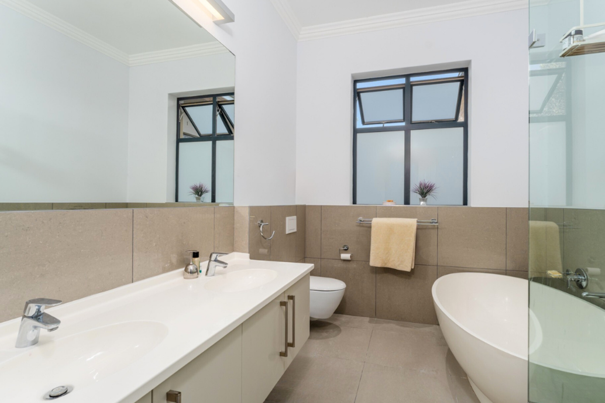 Modern bathroom featuring a double vanity with integrated sinks, a freestanding bathtub, a glass-enclosed shower, and large format neutral wall and floor tiles.