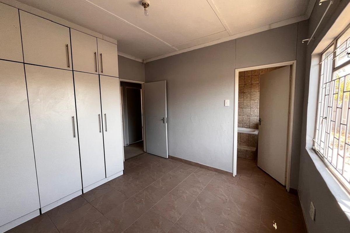 A bedroom featuring built-in cupboards, tiled flooring, and an en-suite bathroom entrance, offering a functional and neutral living space.