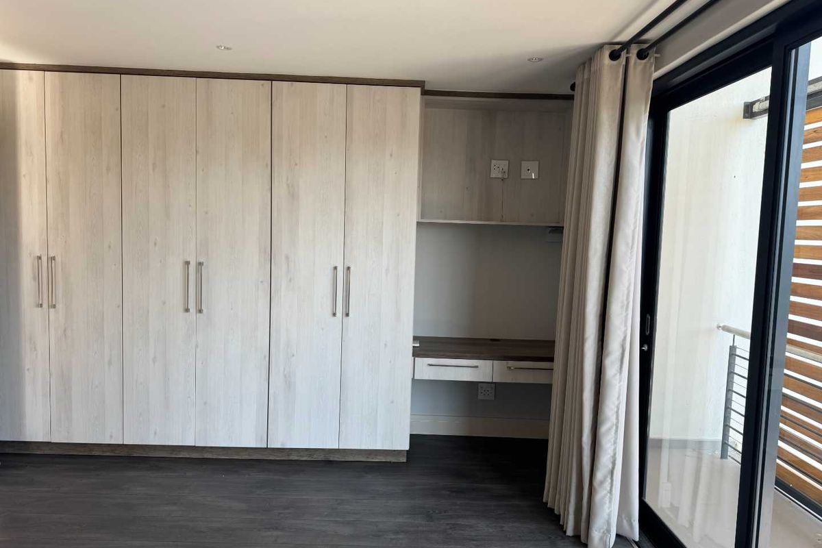 Bedroom featuring built-in light wood cabinetry with an integrated desk area and sliding glass doors leading to an outdoor balcony.