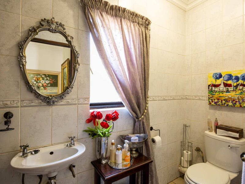 A compact bathroom featuring a wall-mounted basin, dual-handle faucet, and standard toilet, finished with neutral ceramic wall tiles.