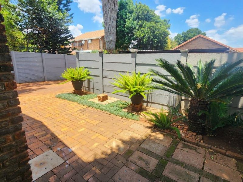 A private rear courtyard featuring brick paving, established garden beds, and secure precast concrete boundary walls.