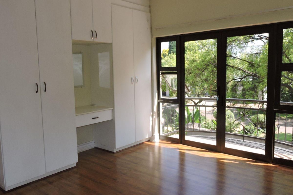 Bright bedroom featuring built-in cupboards with an integrated vanity, laminate flooring, and direct access to a private balcony through large glass doors.