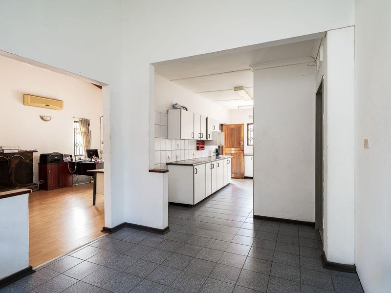 A functional kitchen area featuring tiled flooring, built-in cabinetry with laminate countertops, and a tiled splashback, connecting to an adjacent living space.