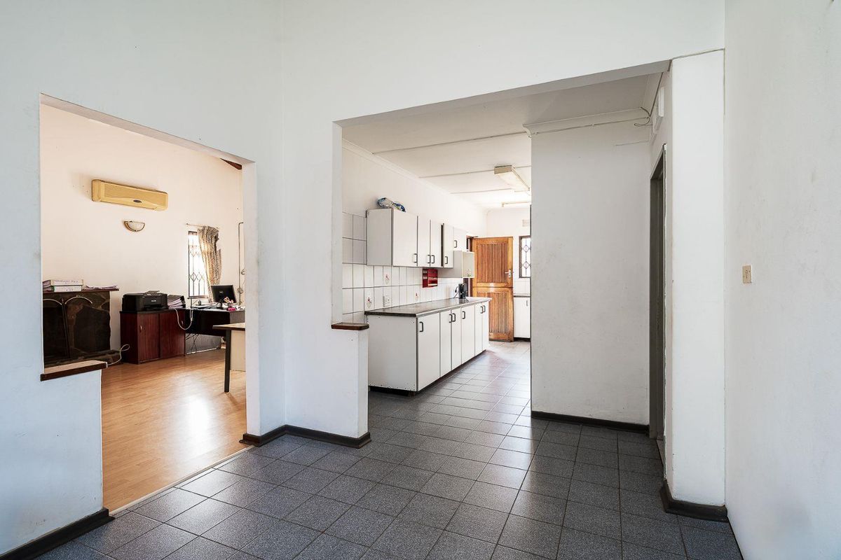 A functional kitchen area featuring tiled flooring, built-in cabinetry with laminate countertops, and a tiled splashback, connecting to an adjacent living space.