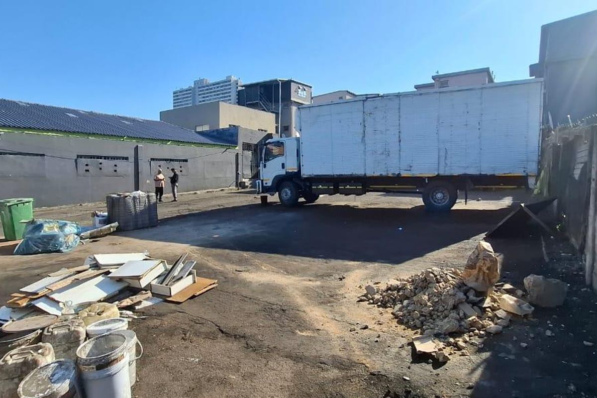 A large, paved industrial yard area featuring a concrete perimeter wall and access to the rear facade of the commercial building.
