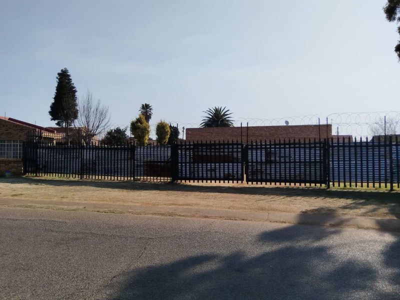 A street-level view of a residential property featuring secure metal perimeter fencing topped with razor wire and a gated entrance.