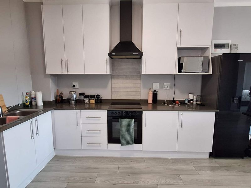 Modern kitchen featuring white cabinetry, stone countertops, integrated electric oven and hob, extractor fan, and durable laminate flooring.