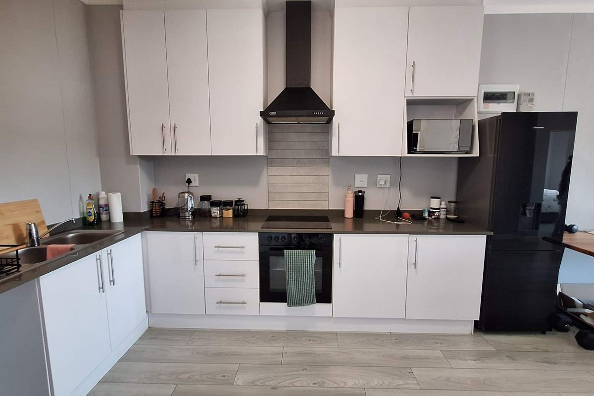 Modern kitchen featuring white cabinetry, stone countertops, integrated electric oven and hob, extractor fan, and durable laminate flooring.