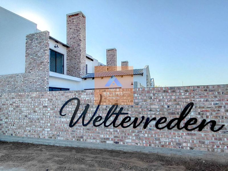 Front view of the Weltevreden townhouse complex featuring a prominent brick boundary wall, chimneys, and modern architectural design.
