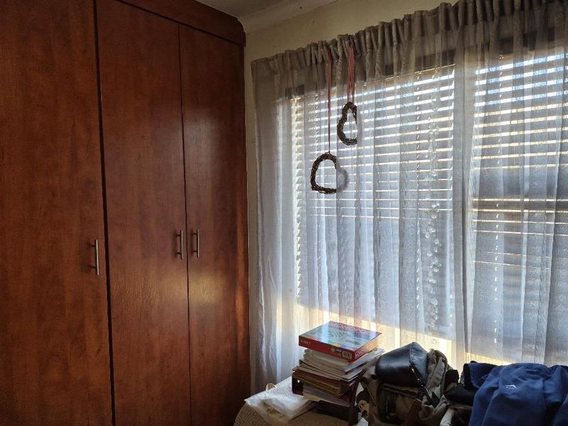 A bedroom featuring dark wood built-in cupboards and window blinds, providing functional storage and natural light control.