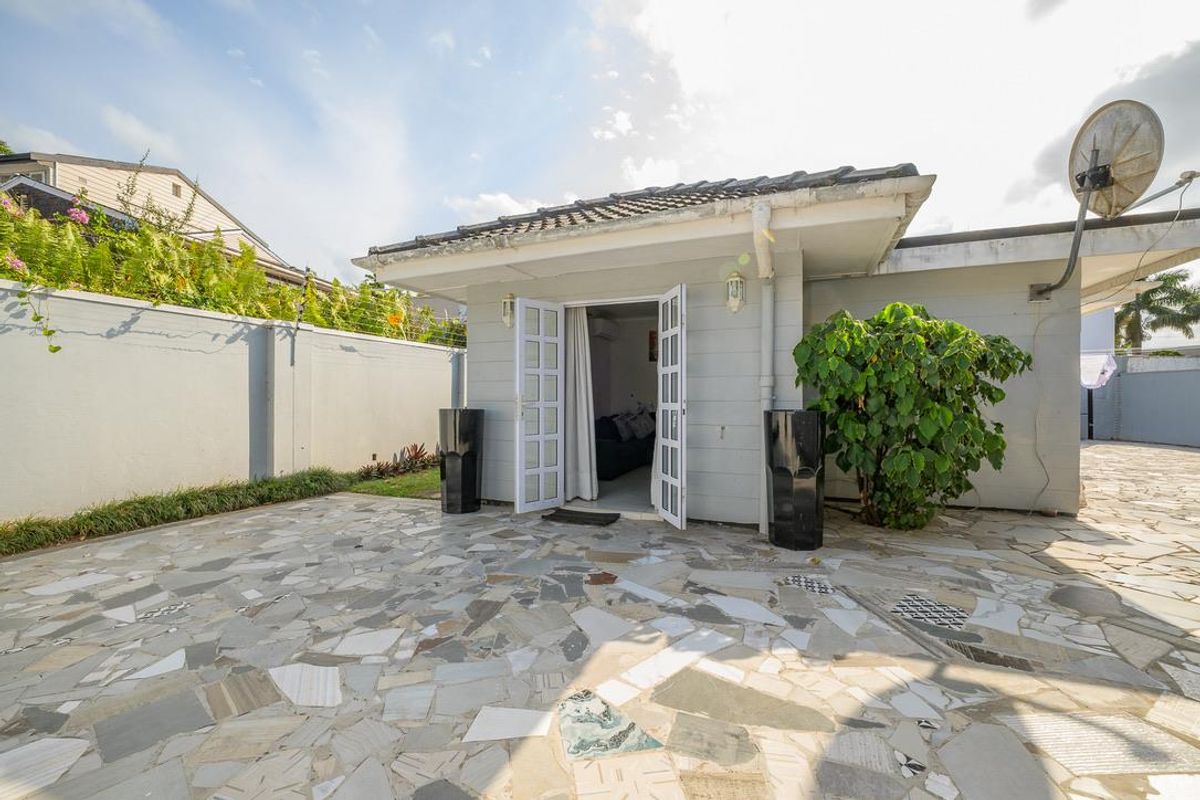 A rear exterior view of the property featuring a paved patio area, double French doors, and a perimeter boundary wall.