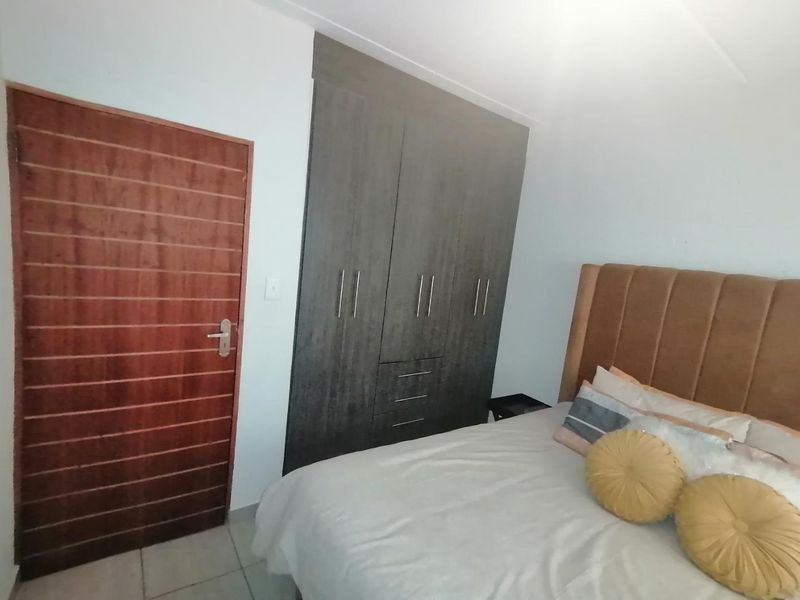 A well-maintained bedroom featuring built-in cupboards, tiled flooring, and a solid wooden door.